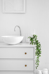 Sink with candles and houseplant on chest of drawers in bathroom