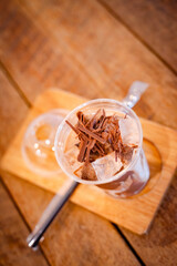Iced chocolate with chocolate chunks on ice in a glass on a wooden coaster