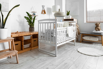 Interior of light children's bedroom with baby crib, table and bench
