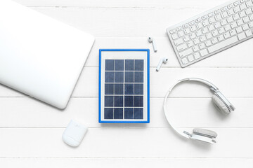 Composition with portable solar panel, wireless earphones, laptop and keyboard on white wooden background