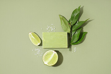 Composition with natural soap bar, lime, sea salt and plant branch on green background