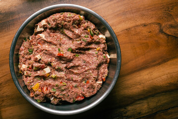 Ground meat dough prepared for homemade hamburger. Ground meat in metal bowl on wooden table.