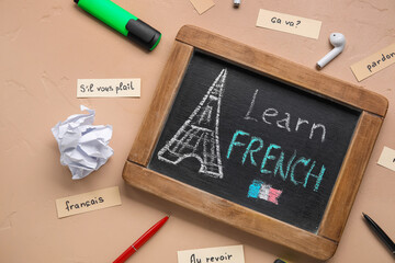Chalkboard with text LEARN FRENCH, stationery, earphones and crumpled paper on beige background