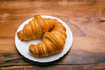 Croissants in white plate on wooden table. Top view.