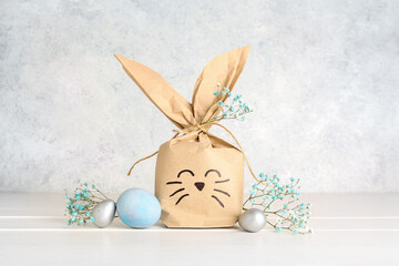 Bunny gift bag, Easter eggs and gypsophila flowers on white wooden table