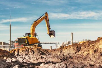 A wheeled excavator in a trench digs the ground. An excavator with a highly raised bucket against a...