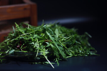Green vegan salad from green leaves mix and vegetables. Fresh arugula leaves in a colander. Black background.