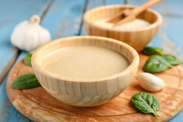 Board with bowl of tasty tahini, sesame seeds, spinach and garlic on color wooden table, closeup