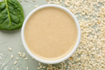 Bowl with tasty tahini, sesame seeds and spinach on grunge background, closeup
