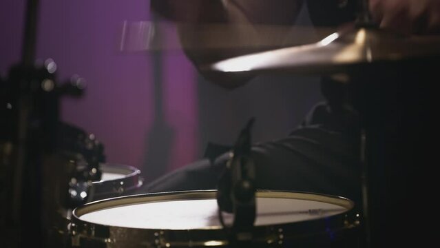 A young Caucasian man drummer plays a drum kit in a music studio. Creates music and art. Drum set, drum kit in dark, drummer plays. The rock band is rehearsing, studying. The musician is playing