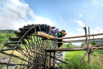 Ethnic minority girl beside a bamboo waterwheel collects water from a stream to irrigate rice fields. Special landscape of the mountains of Cao Bang province, Vietnam.