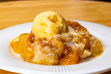 View of juicy homemade delicious peach cobbler with a scoop of vanilla ice cream.