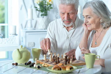senior man looking at chess board while drinking tea at home