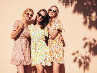 Three young beautiful smiling hipster female in trendy summer dresses clothes. Sexy carefree women posing in the street. Positive models having fun, talking, chatting. Going crazy. In sunglasses