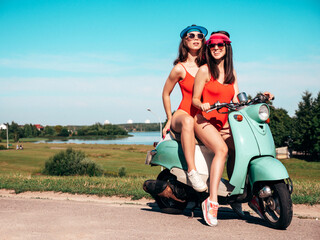 Two young beautiful smiling hipster female in summer red bathing suits. Sexy carefree women driving retro motorbike. Positive models having fun, riding classic Italian scooter. In swimwear