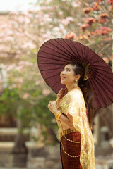 asian woman holding bamboo umbrella standing against plumeria flower blooming in old temple ayutthaya thailand