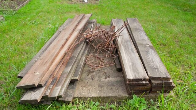 Wet boards and rusty iron bars on the street are surrounded by green grass. Remains after the construction of formwork and reinforcement. The camera flies smoothly over the construction waste