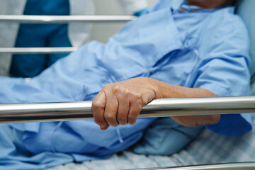 Asian elder senior woman patient holding bed rail while lie down with hope waiting her family in hospital.