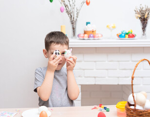 Child boy decorating and painting easter eggs against defocused fireplace with Easter decorations...