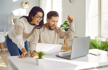 Family couple getting excited about success when they get email with excellent job offer. Happy young man and woman reading good news and looking at laptop computer with very excited face expressions