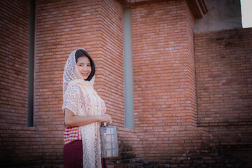 Beautiful thai girl in traditional thai dress covered with a white cloth standing and looking to to...