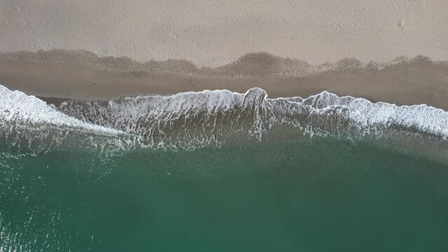 Aerial lookdown of soothing aqua blue sea waves hitting beach sand drone view