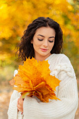 Cute fashion pretty tender woman with curly hair in fashion vintage knitted sweater holds a yellow maple leaves in the golden park