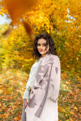 bright beautiful autumn girl with a curly hairstyle in a fashionable coat and sweater walks in an autumn park with yellow foliage on a sunny day