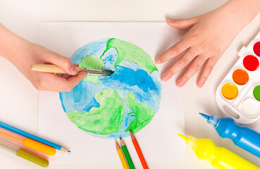 The child draws the planet with a brush and paints on a white surface.