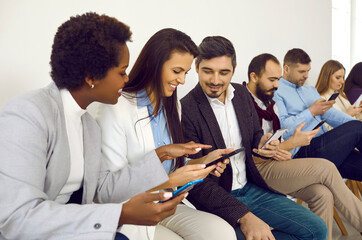 Group of different people sitting in row, using modern cellphones, looking at memes, reading or...