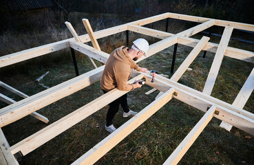 Man worker building wooden frame house on pile foundation. Carpenter installing wooden board, using...
