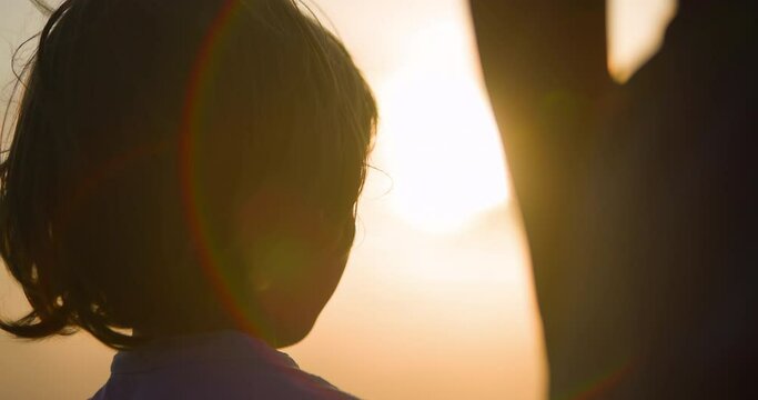 Close up the beautiful cute face of a boy with blonde hair and blue eyes. The cute boy smiles and looks at his sister. A child at orange sunset turns around and looks up. Smiling face of Caucasian boy