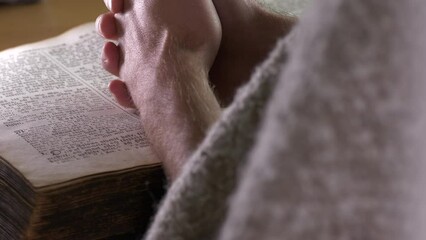 Hands of a Caucasian friar praying over a bible. Back static view