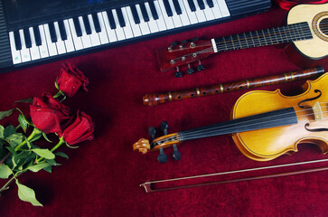 Naklejka premium Synthesizer keyboard, violin, guitar, pipe, a bouquet of red roses on a table with a burgundy tablecloth.