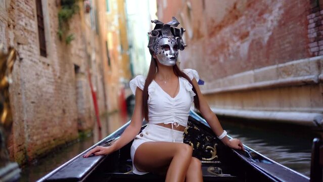 Beautiful woman in white dress with carnival mask riding on gondola, Venice, Italy