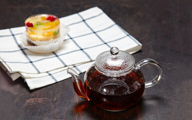 Black tea in a glass teapot and cake with jelly on wooden background. Yummy mini dessert and traditional tea on breakfast, closeup