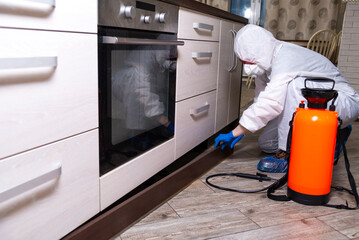 An exterminator in work clothes sprays pesticides with a spray gun. Fight against insects in apartments and houses. Disinsection of the premises