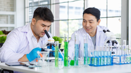 Asian professional male scientist researcher in white lab coat and rubber gloves sitting using...