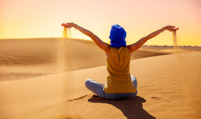 Woman tourist in Sahara desert at sunset having sand in her hands