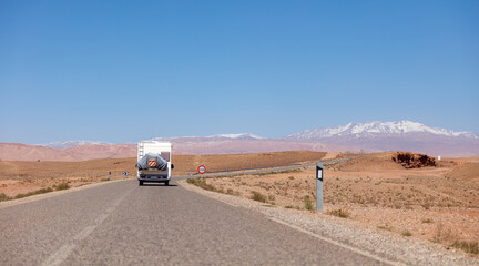Road trip in Morocco- Asphalt road with driving motor home and mountain atlas in the background