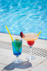 Two colorful cocktail glasses at the edge of swimming pool