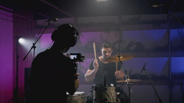 Shooting a music video. The director of photography makes a video, shoots a drummer musician. The view behind the scenes. Create a music video for a rock band. Creative director and crew.