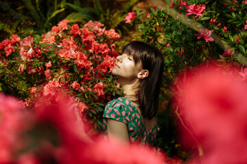 Naklejka premium Beautiful girl in a green dress in a garden of blooming azaleas