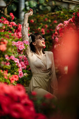 A woman in glasses in a light dress in a garden of flowers