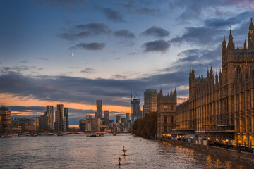 Obraz premium Beautiful view of Parliament buildings, river Thames and city buildings in London, England, at sunset with rising moon