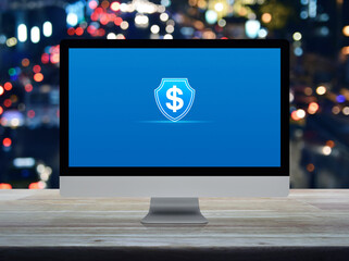 Dollar with shield flat icon on desktop modern computer monitor screen on wooden table over blur colorful night light traffic jam road in city, Business money insurance and protection online concept