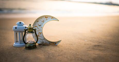 Vintage lamp and a white lantern lamp along with a crescent moon in a sea side with sunset, Ramadan and Eid concept Selective focus