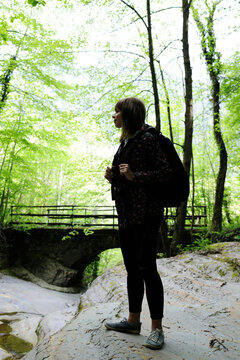 Full length of woman with backpack looking at view while standing on rock in forest