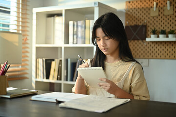 Concentred teenage asian woman doing homework, school project, preparing for exam at home