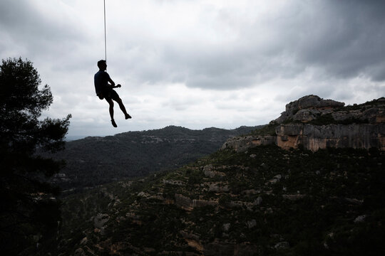 Silhouette man hanging on rope over mountains against cloudy sky during sunset